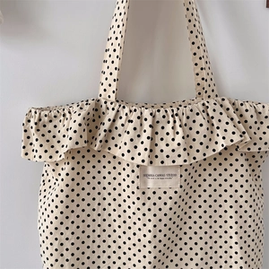 Close-up of cream canvas tote bag featuring polka dots, ruffle edges and woven brand label