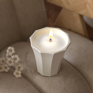 Macro detail of a faceted white ceramic candle holder with a burning wooden wick