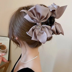 Close-up of pink silk bow hair claw clip with crystal center for elegant hairstyling