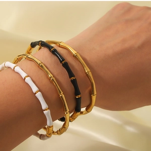 Close-up of stacked gold, black, and white bamboo-style bangles on silk background
