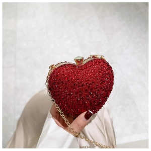 Detail showing hand holding heart-shaped red rhinestone clutch with gold chain strap