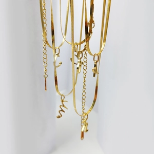 Detail of gold letter pendants and layered snake chains in polished stainless steel