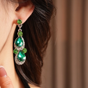 Detailed close-up of vintage silver earrings with green pear-shaped gemstones on a model