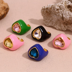 Close-up of five colorful enamel heart rings with crystal centers on a textured stone