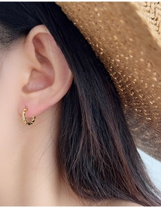 Close-up of gold-plated twisted rope hoop earrings worn on a woman's earlobe
