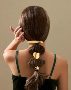 Detail shot of golden star and heart metal hair clips styled on model's ponytail