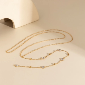 Collana dorata elegante con strass e perle minimaliste su uno sfondo beige chiaro