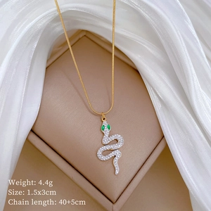 Macro view of gold snake pendant with green gem eyes and crystals on silk background