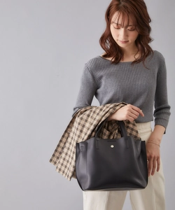 Detail of a medium black PU leather tote bag with a round metal buckle and side fold design