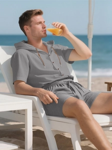 Men's grey linen short set with buttoned hoodie on a tropical beach vacation chair