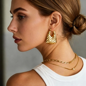 Close-up of golden geometric earrings with pleated texture on model for minimalist style