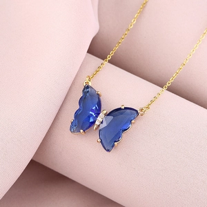 Detail of blue crystal butterfly pendant on gold chain against pink fabric background