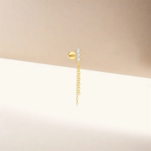 Détail d'une boucle d'oreille en chaîne dorée avec trois zircons blancs et une chaîne pendante