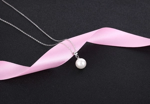 Detailed view of elegant white pearl pendant on fine silver chain with pink ribbon decor