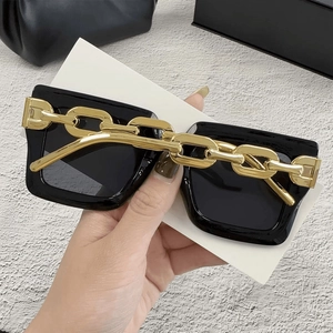 Detalle de gafas de sol cuadradas de gran tamaño con cadena dorada en montura negra