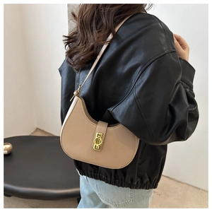 Close-up of beige crescent shoulder bag with gold ring buckle worn by a model