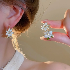 Close-up of elegant floral earring with white enamel petals and gold leaf detail