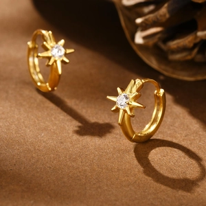 Detailed close-up of golden stainless steel star huggie earrings with a sparkling zircon