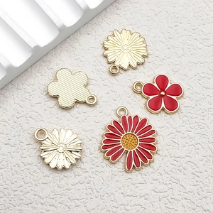 Macro shot of red enamel and gold flower charms for DIY jewelry making on white surface