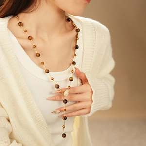 Detailed view of long gold tassel necklace featuring tiger eye beads and leaf pendant