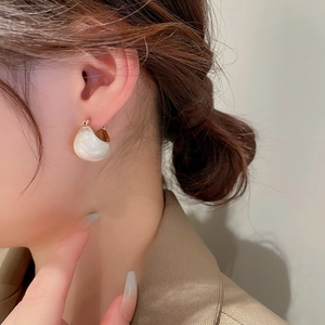 Macro view of C-shaped gold-plated hoop earrings with pearlescent white resin on model