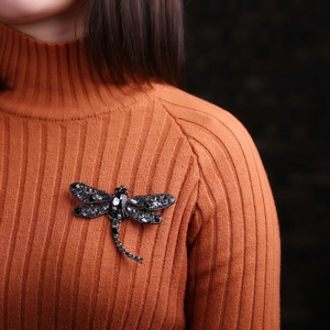 Close-up of a dragonfly brooch with black crystals pinned on an orange knit sweater