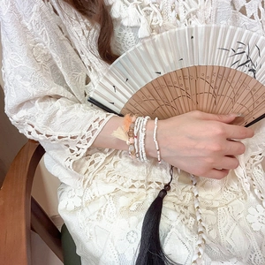 Detail of bohemian multilayer beaded bracelet featuring soft orange and cream tassels