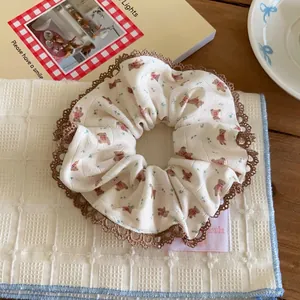 Detail of cream cotton scrunchie with cute bear print and brown lace trim on checkered cloth
