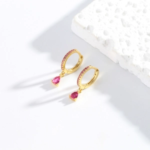 Macro view of gold hoop earrings featuring pink pear-cut crystals and sparkling stones