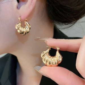 Detail showing classic golden croissant hoops with a polished metallic texture and twist design