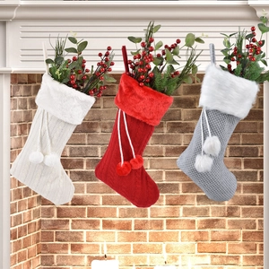 Trois chaussettes de Noël tricotées en rouge, blanc et gris devant une cheminée