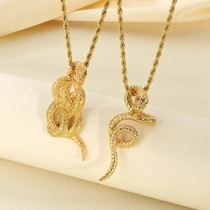 Macro detail of 18k gold plated snake pendants with red gemstone eyes on beige fabric