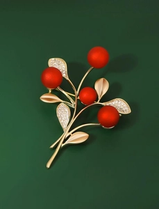 Detailed close-up of sparkling plant brooch with red berries and gold leaf texture