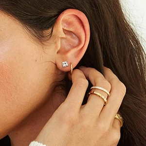 Detailed view of layered 925 silver geometric stud earrings and stacked gold rings with gems
