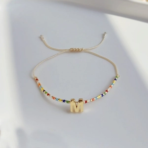 Detailansicht eines bunten Boho-Perlenarmbands mit goldenem M-Buchstaben und verstellbarer Kordel