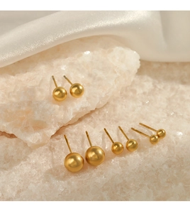 Macro detail of various sizes of gold stainless steel ball stud earrings on white crystal