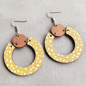 Detail view of Bohemian wood earrings with yellow polka dots on a grey concrete surface