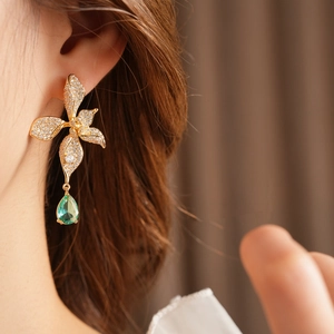 Macro detail of vintage gold flower earring with clear zircons and green teardrop stone