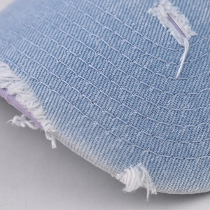 Macro detail of washed light blue denim brim with white stitching and distressed edges