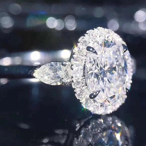 Anillo de cristal ovalado con halo y piedras laterales de pera en banda de metal plateado