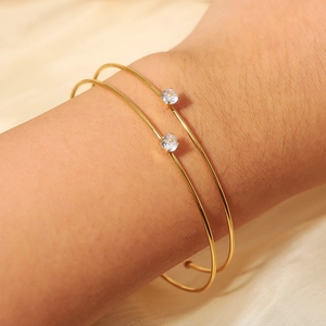 Detail of two minimalist gold-plated bangles with brilliant round crystals on silk background
