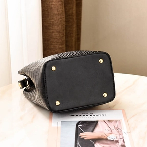 Black crocodile pattern bucket bag with golden feet studs shown on marble surface