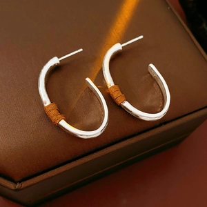 Close-up of matte silver oval earrings with brown rope wrap on dark leather case