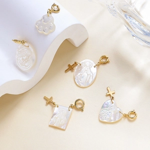 Macro shot of white shell pendants in heart and cat paw shapes with gold metal ring hooks