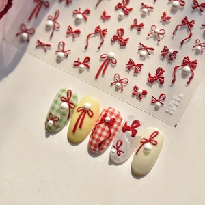Detail of red bow and white pearl 3D nail stickers with festive checkered patterns