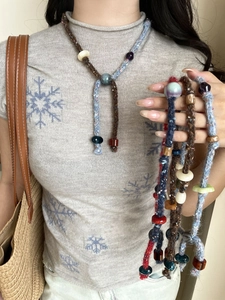 Detail of bohemian cotton rope necklaces with resin beads on a grey snowflake sweater