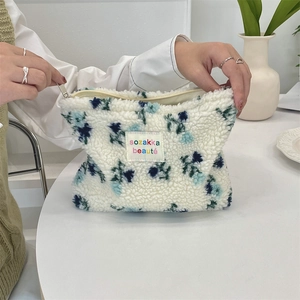 Close-up of hand opening the zipper on the floral plush fleece makeup storage bag