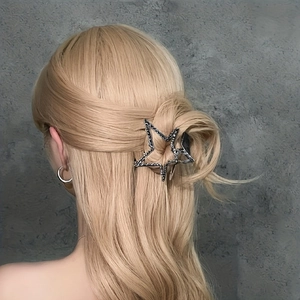 Dettaglio di una grande molletta a stella nera che fissa i capelli biondi di una donna