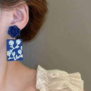 Detail of blue rose stud earrings with white floral pendant on a model's ear
