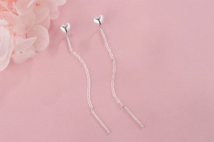 Detailed view of S925 silver long tassel heart earrings on a soft pink background